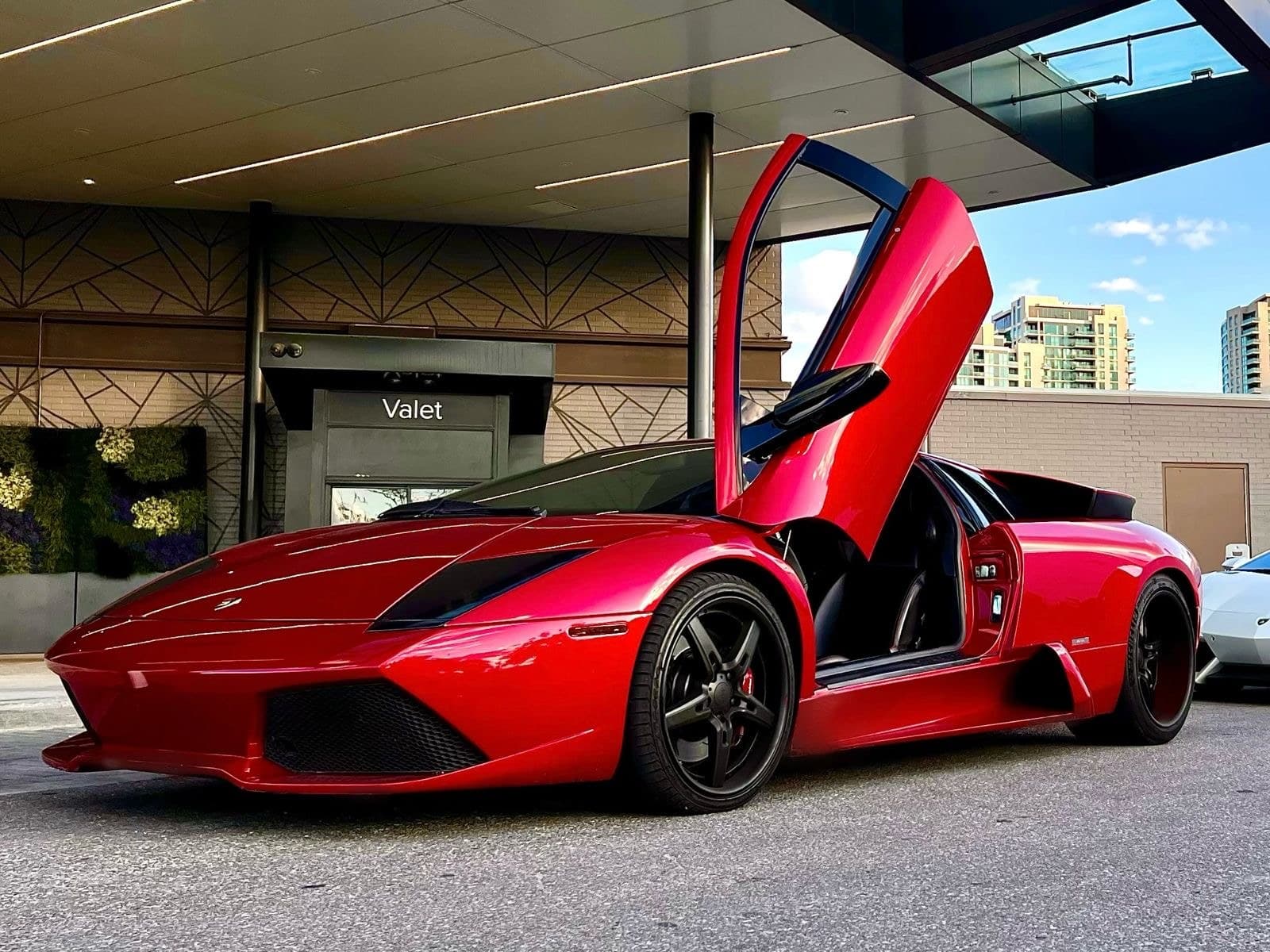 2004 Lamborghini Murciélago in red with its scissor door raised at a valet stand, for sale from DDE Rentals