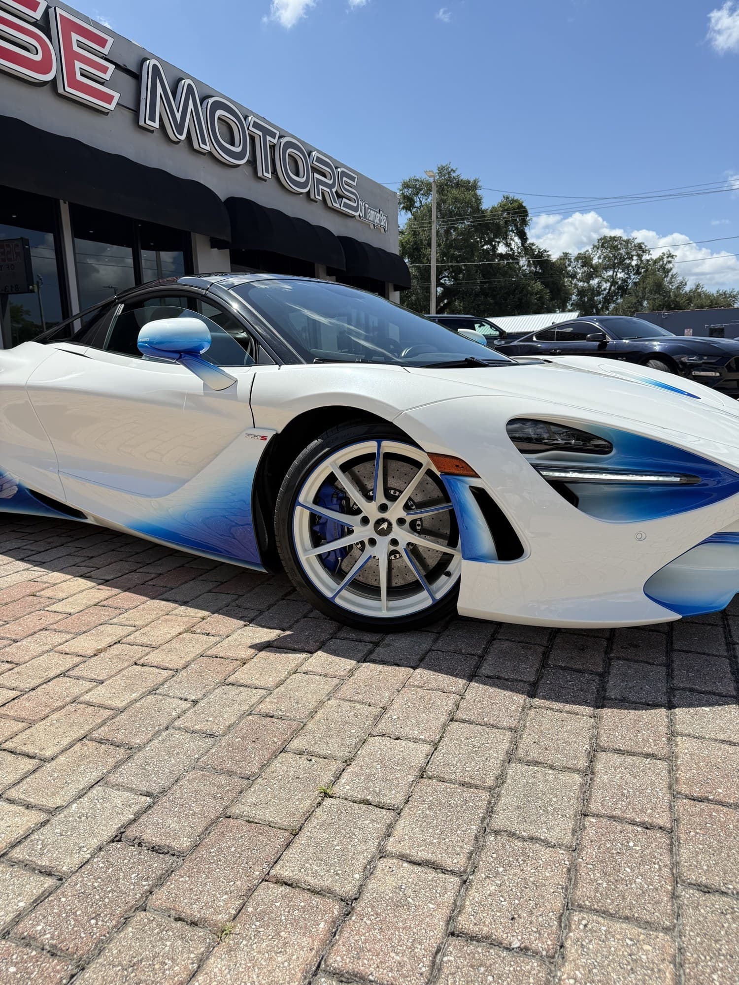 Front three-quarter detail of the 720S Spider showing the blue-fade aero blades, white wheels, and blue calipers over carbon-ceramic brakes